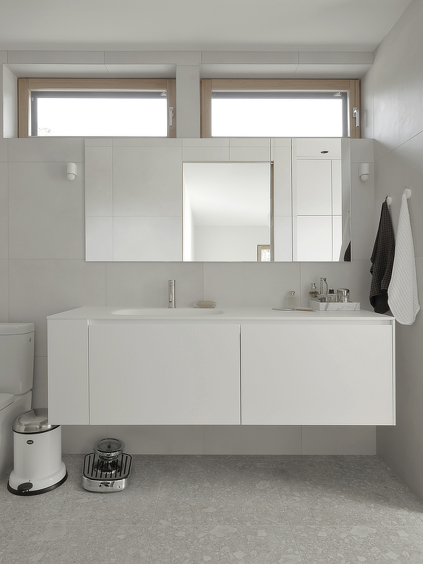 Kylpyhuoneessa on minimalistiset valkoiset kalusteet ja terazzo laatat sekä nauhaikkunat ison peilin yläpuolella.
