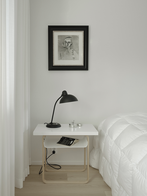 Makuuhuoneessa on sängyn vieressä kaunis yöpöytä jolla on valaisin ja seinällä taulu yöpöydän kohdalla.
