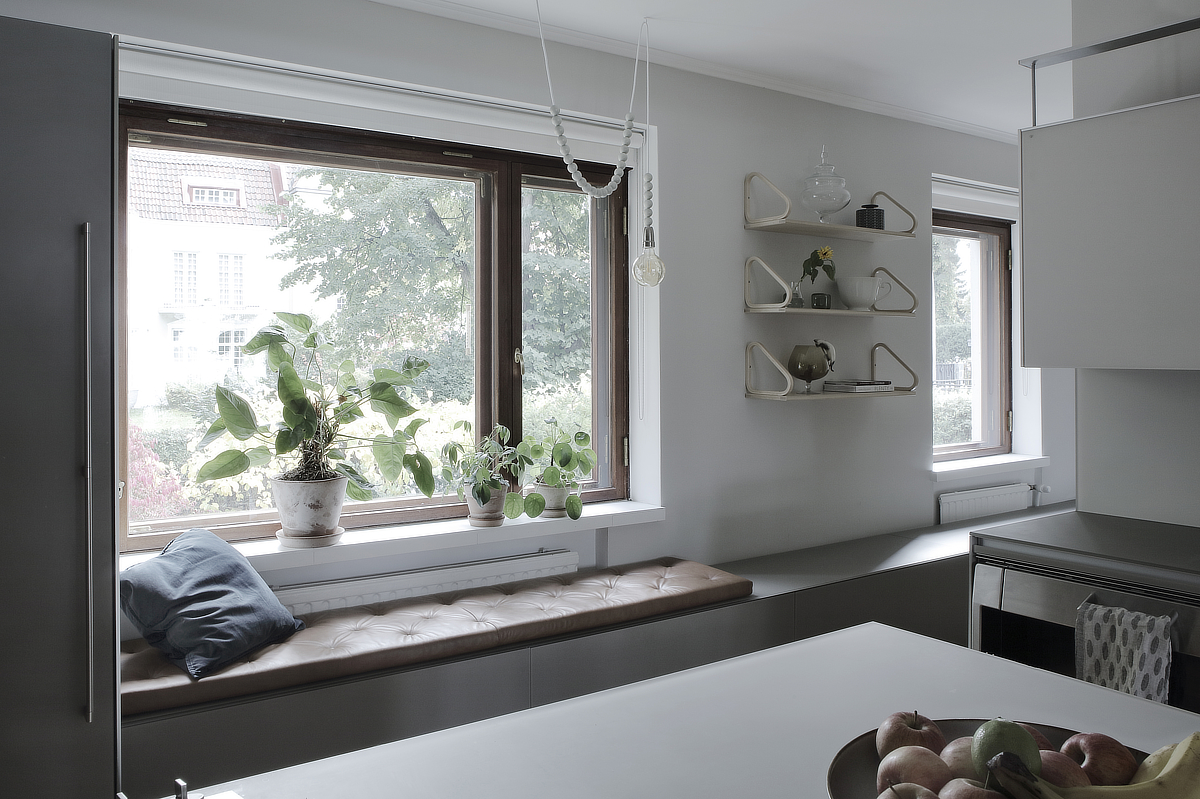 Helsinkiläisen omakotitalon modernin keittiöön tuotiin sisustuksellisuutta lisäämällä avohyllyt ja teettämällä istuinpenkille istuinpehmuste sekä sijoittamalla ikkunalaudalle viherkasveja.